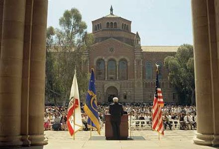 UCLA Chancellor Albert Carnesale addresses a large crowd gathered outside Royce Hall following the Sept. 11, 2001, attacks, standing at a podium framed by the U.S., California and UCLA flags.