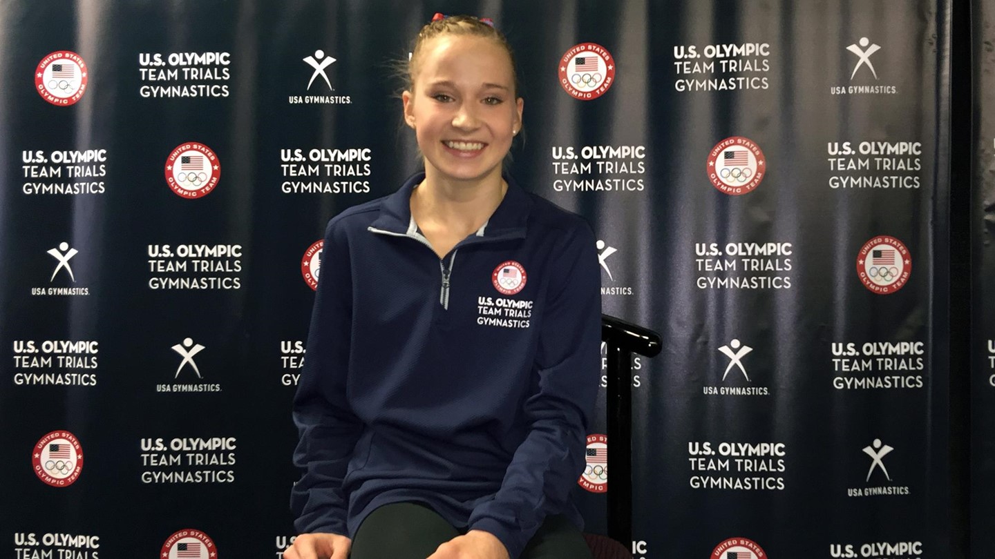 Madison Kocian sits in front of an Olympic Trials banner