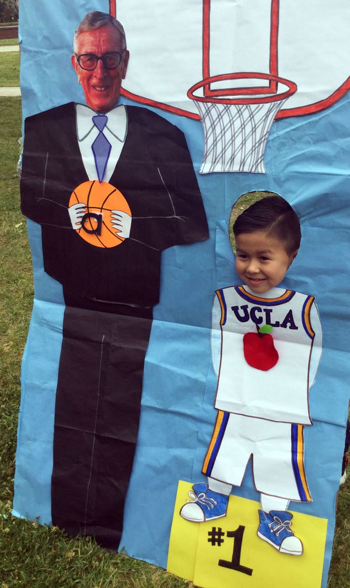 A preschooler poses with a drawing of Coach John Wooden