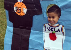 A preschooler poses with a drawing of Coach John Wooden