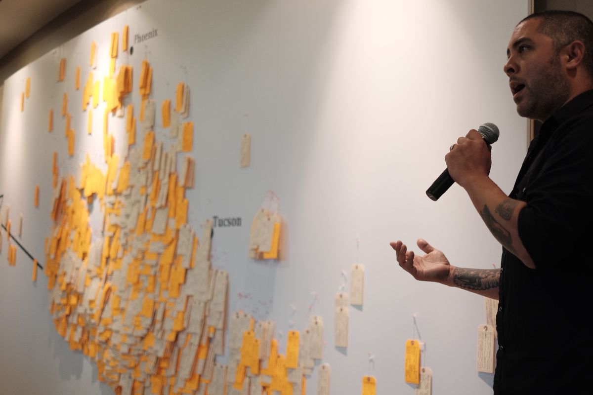 Jason De León speaking into microphone with large white board and stickies in background