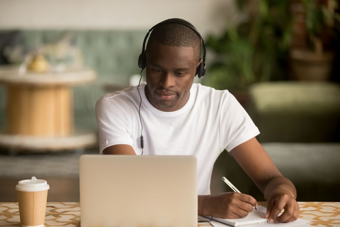 Man with headphones looking at laptop and taking notes