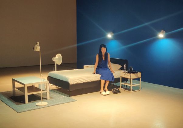 In the LAUREN series, artificial intelligence is replaced with human intelligence. Woman sitting on bed in room