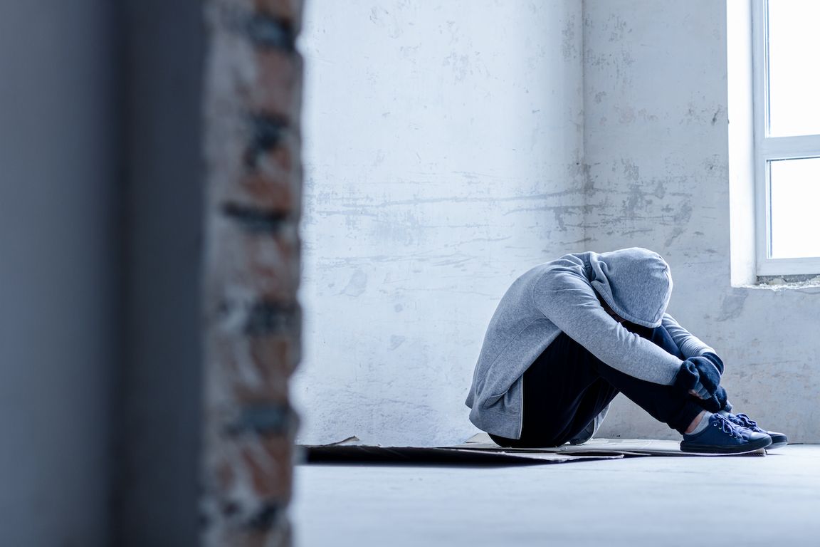 Man in hoodie with head down, sitting in empty room