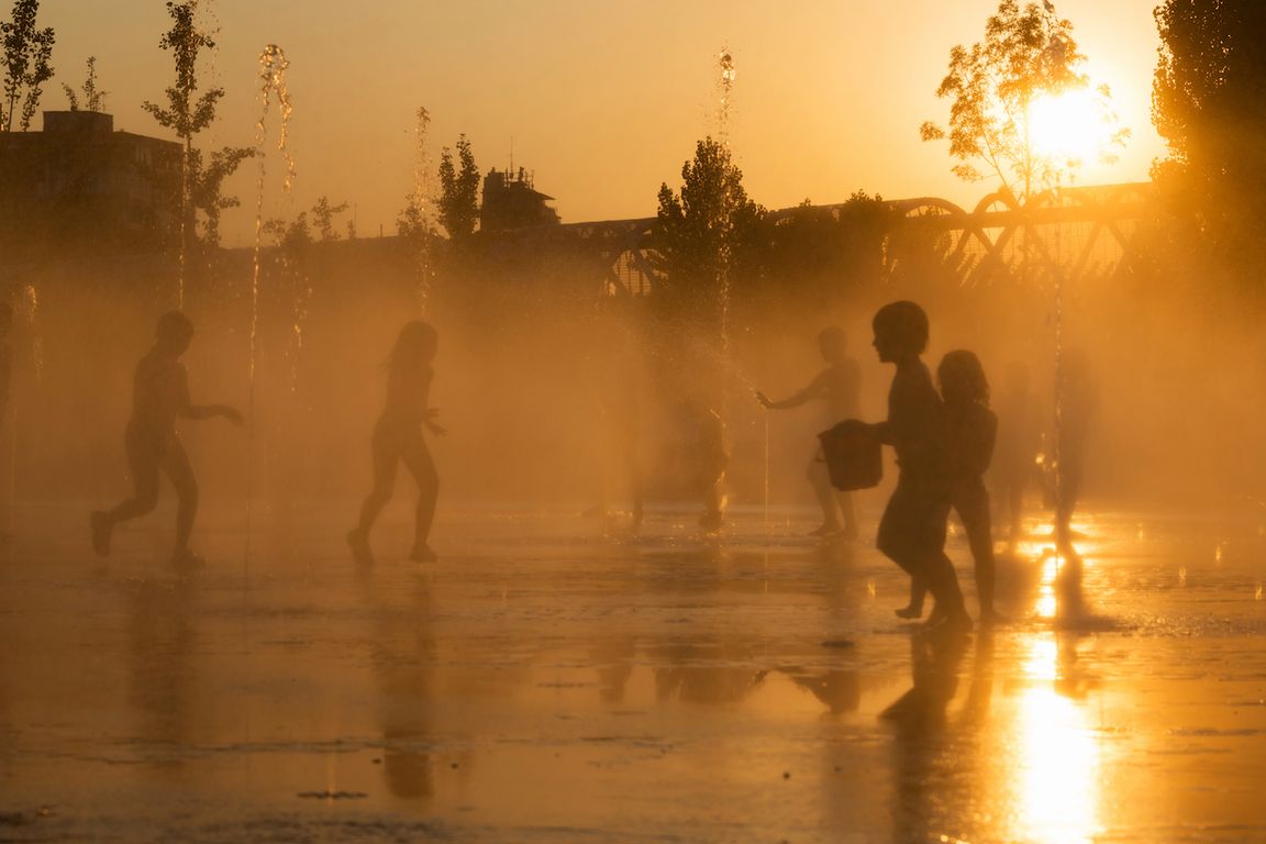 Silhouetted children playing with water as bright sun sets