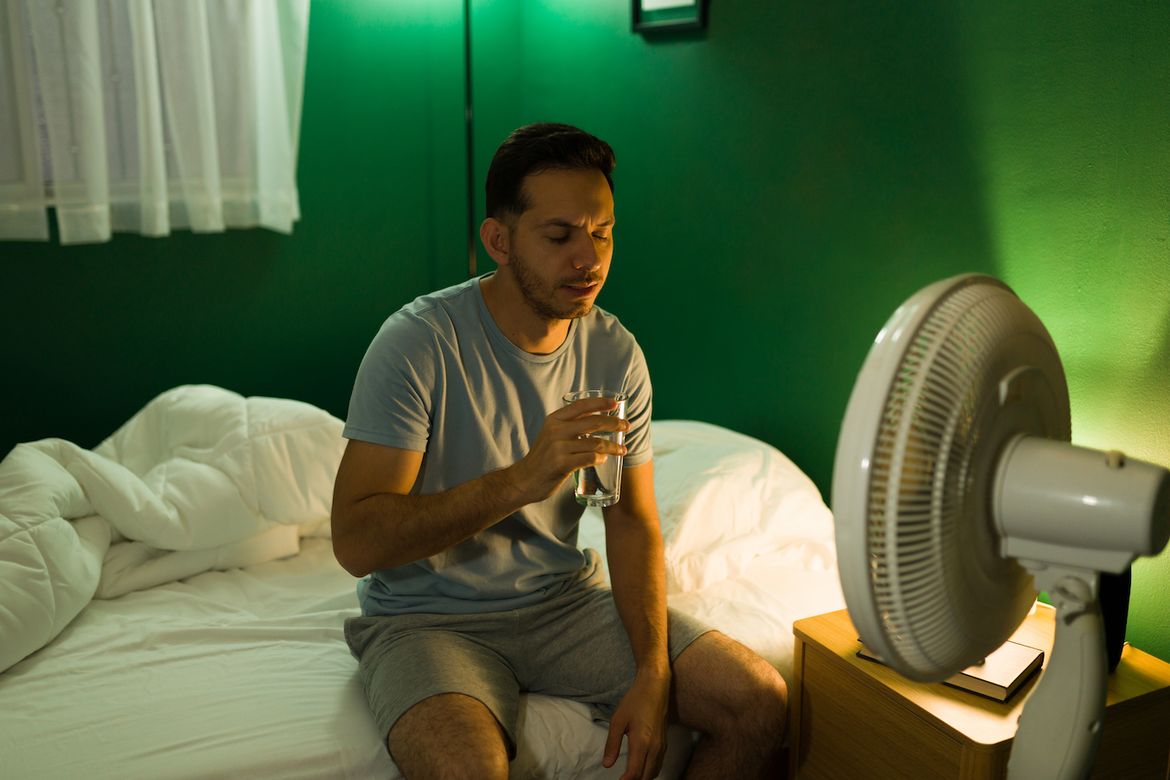 Man with fan and glass of water in bed