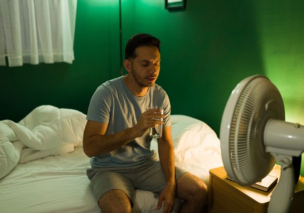 Man with fan and glass of water in bed