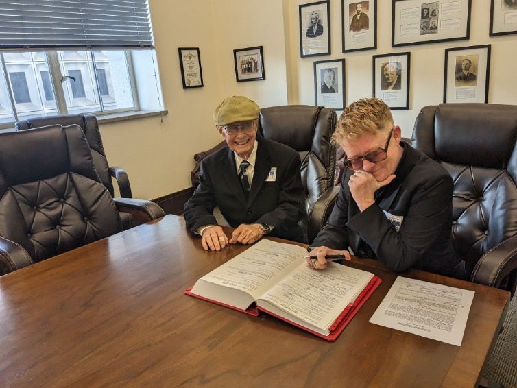 Kelly Besser, right, signing a book as she sits next to her father