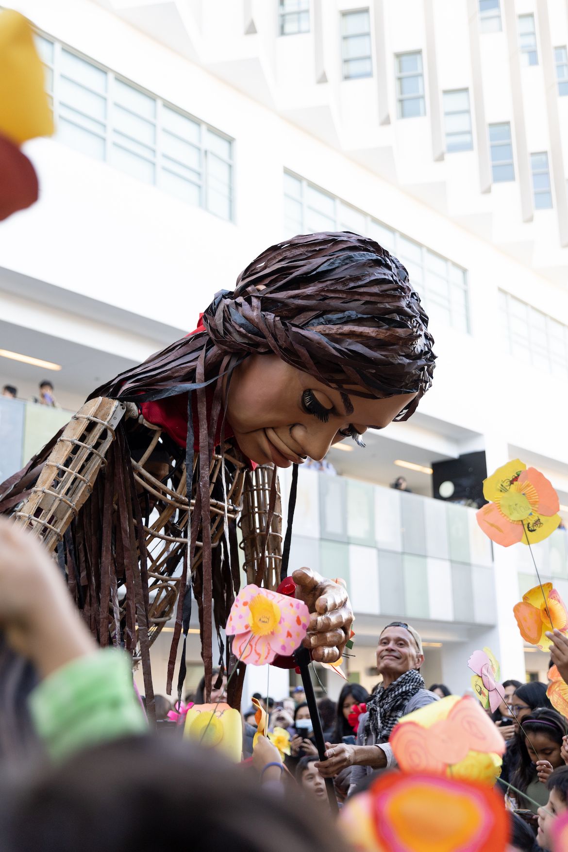 Giant puppet ‘Little Amal’ bends down to touch paper poppies offered by students