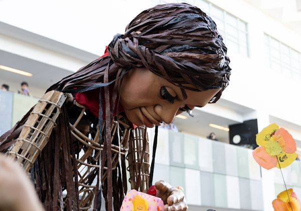Giant puppet ‘Little Amal’ bends down to touch paper poppies offered by students
