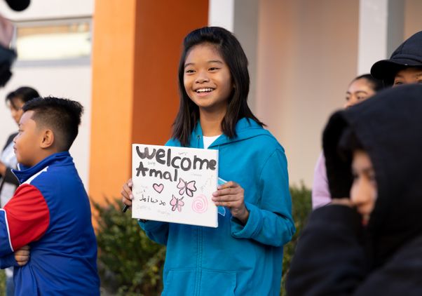 UCLA Community School student in blue hoodie holds sign reading ‘Welcome Amal’