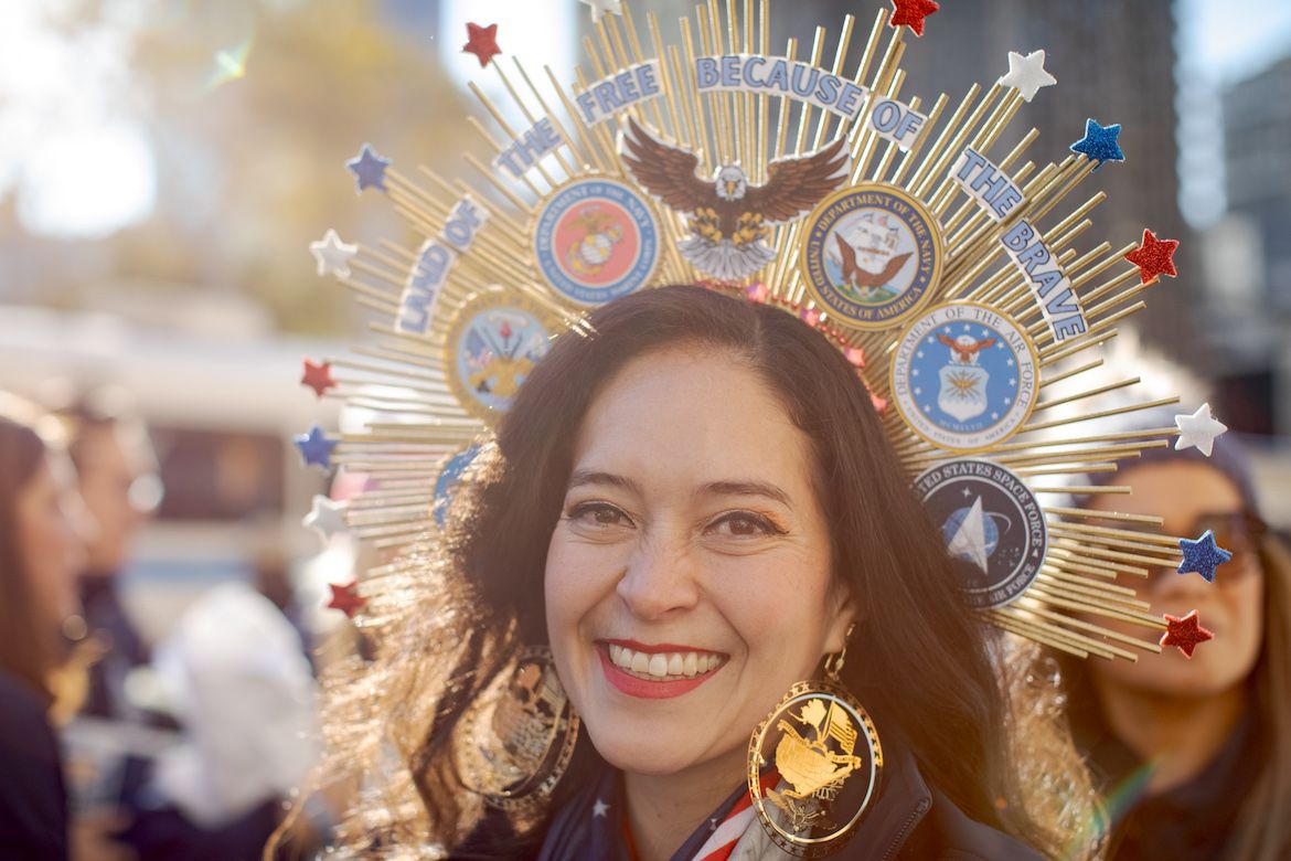 Smiling woman with a crown reading ‘Land of the free because of the brave’ at New York City Veterans Day parade