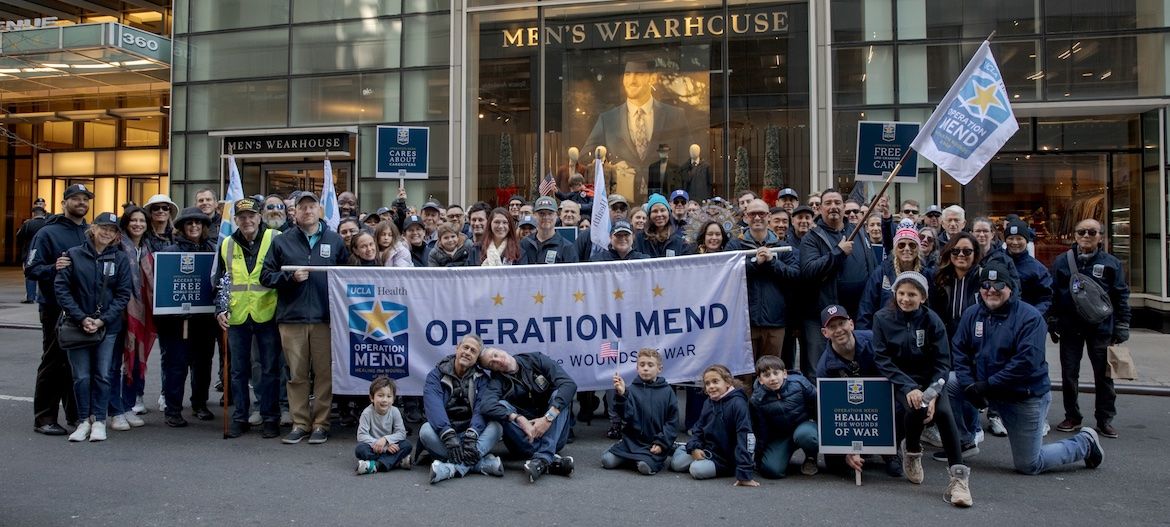 Large group of people pose behind and in front of Operation Mend banner at the New York City Veterans Day parade