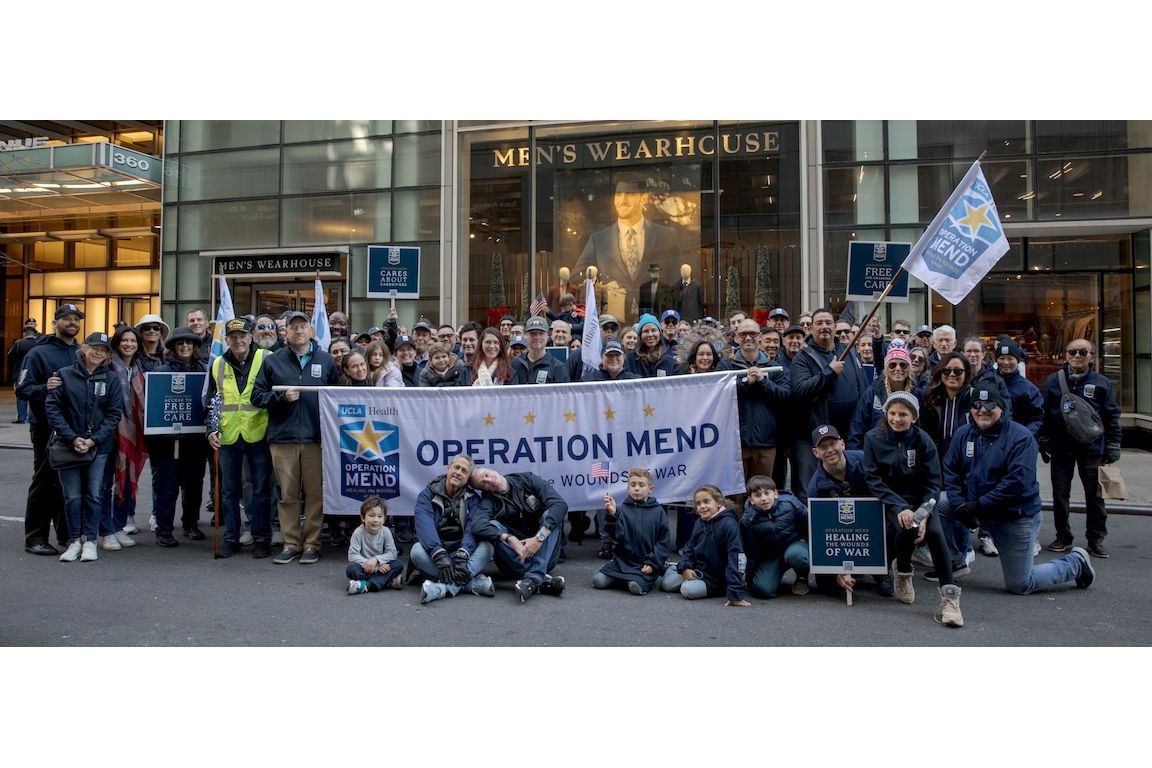 Large group of people pose behind and in front of Operation Mend banner at the New York City Veterans Day parade