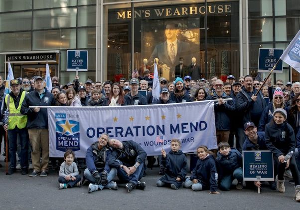 Large group of people pose behind and in front of Operation Mend banner at the New York City Veterans Day parade