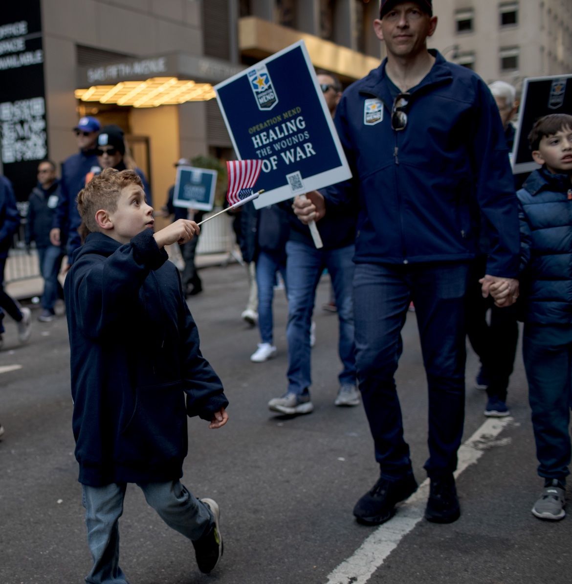 A young boy waves an American flag while marching with the Operation Mend contingent in the New York City Veterans Day parade