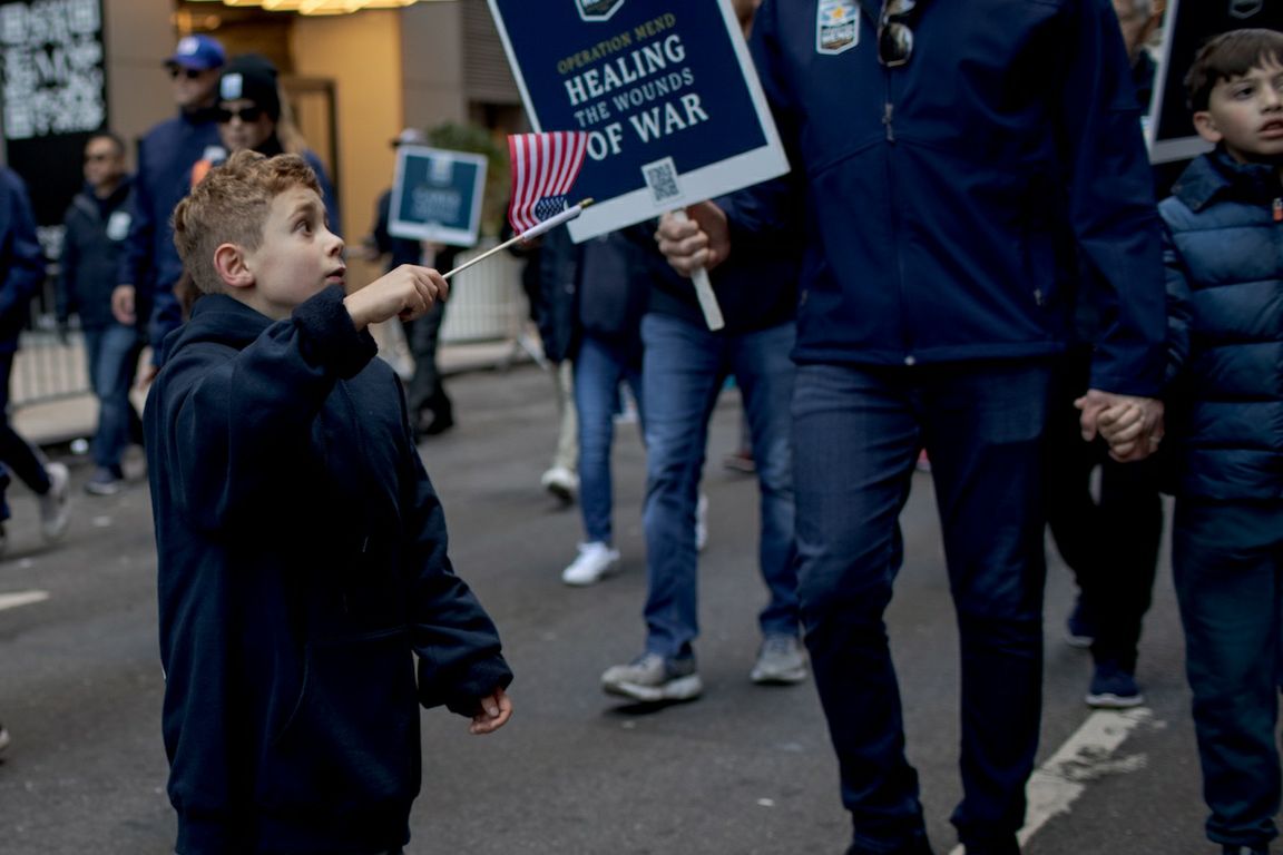 A young boy waves an American flag while marching with the Operation Mend contingent in the New York City Veterans Day parade