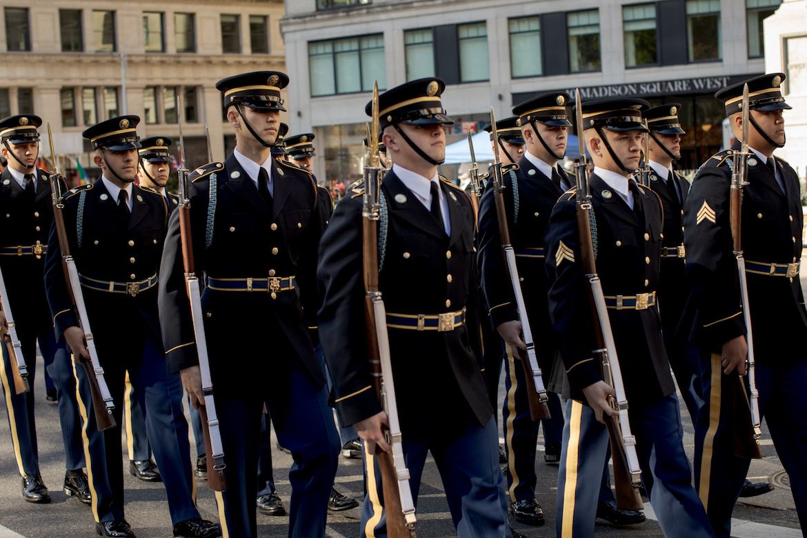 Military members in dress blues, holding rifles, march in the New York City Veterans Day parade