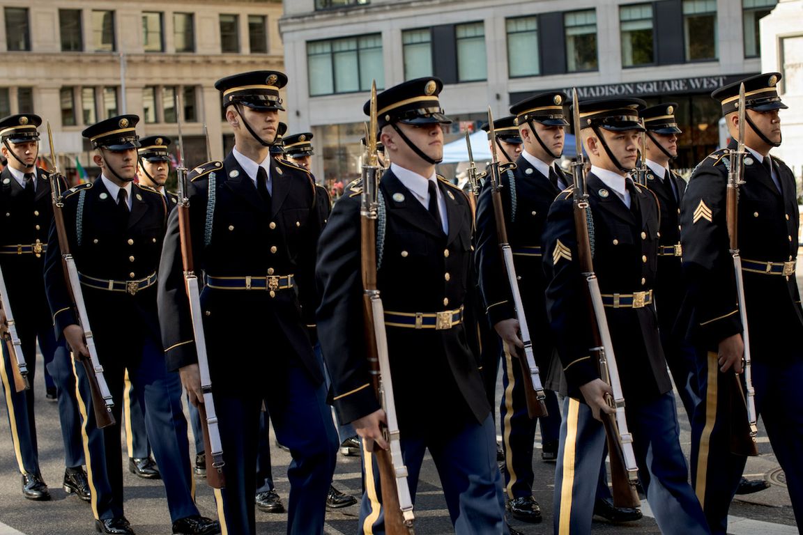 Military members in dress blues, holding rifles, march in the New York City Veterans Day parade