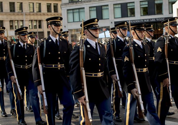 Military members in dress blues, holding rifles, march in the New York City Veterans Day parade