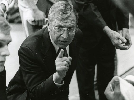 John Wooden leaning over sideline bench and pointing (black-and-white)