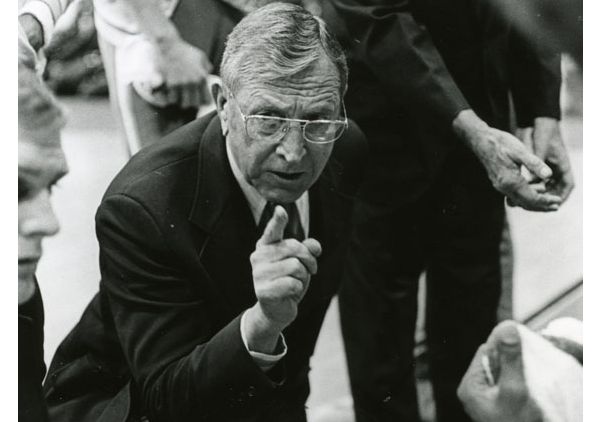 John Wooden leaning over sideline bench and pointing (black-and-white)