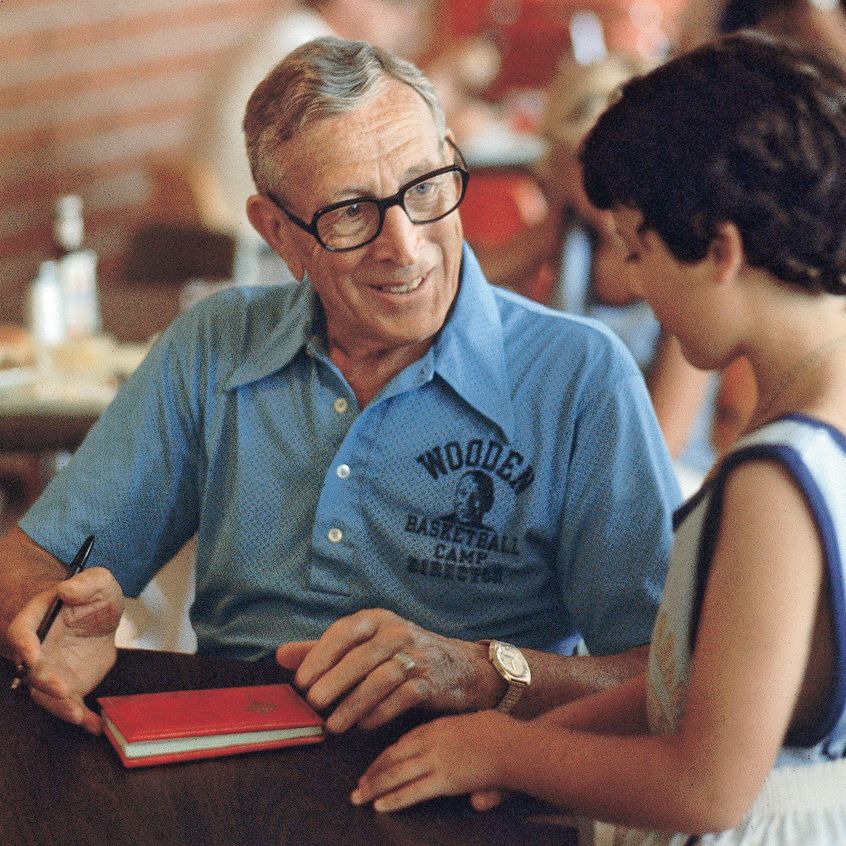 Wooden speaks with a young boy at basketball camp
