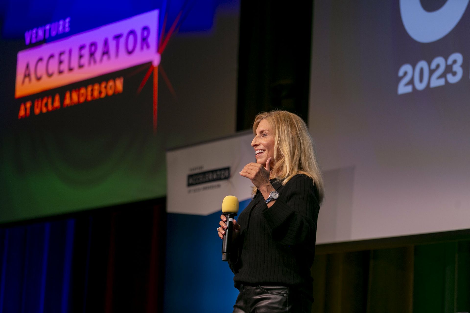 Trish Halamandaris on stage with microphone; sign reading "Venture Accelerator at UCLA Anderson" in the background 
