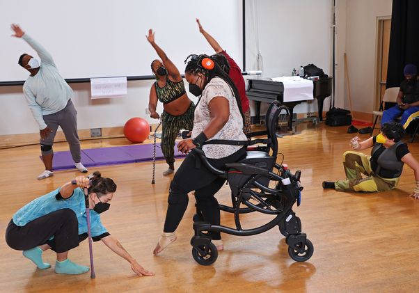 Disabled dancers in motion, some with raised arms, one standing with a walker