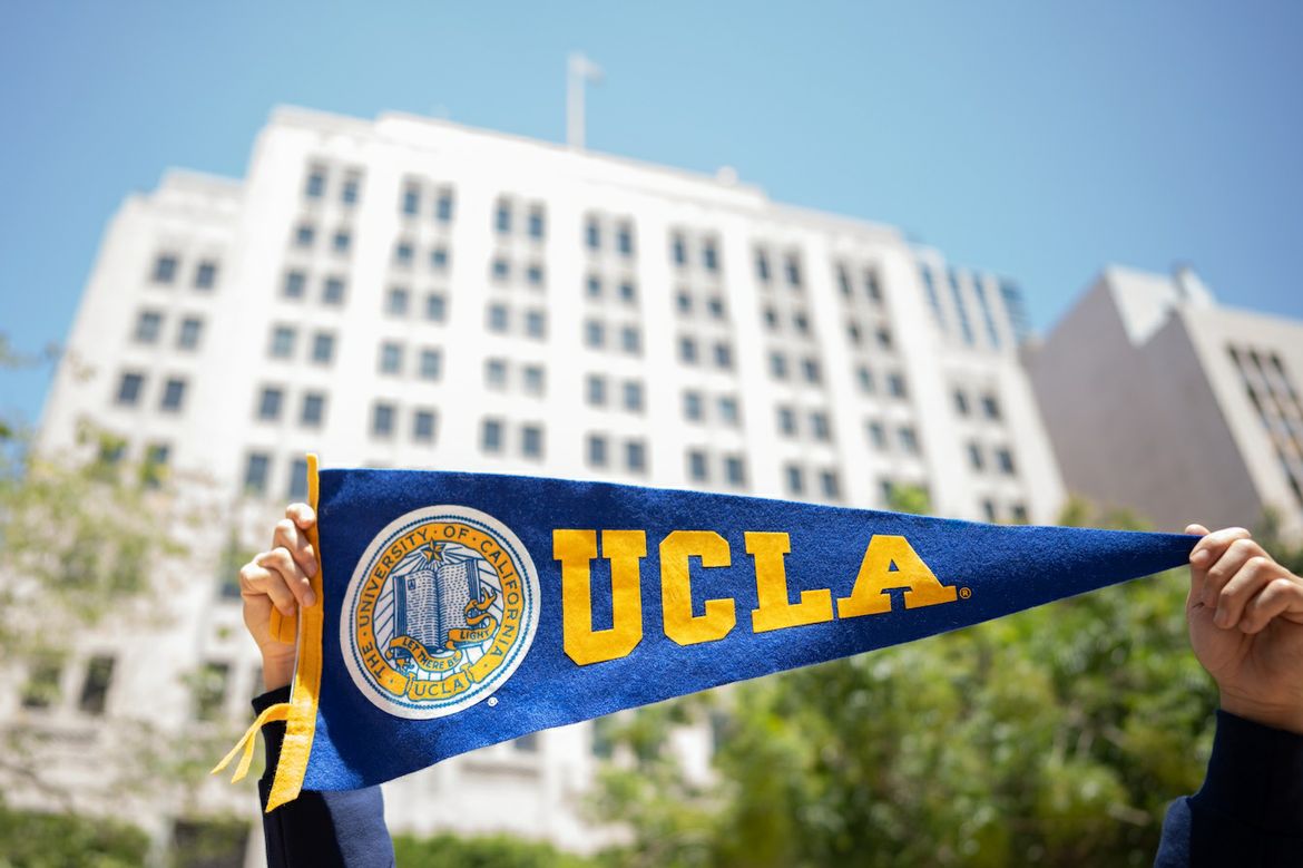 Hands holding up UCLA banner in front of Trust building.