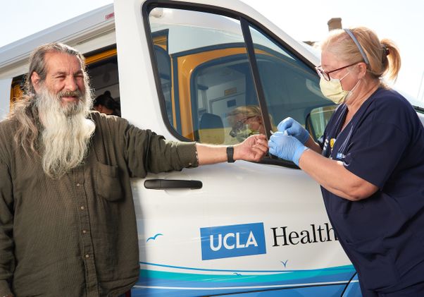 Patient receiving care from UCLA Health Homeless Healthcare Collaborative worker in front of van