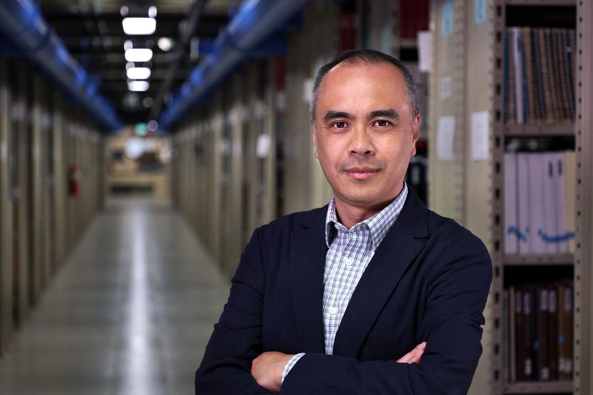 Carlo Medina standing between stacks of books and other media