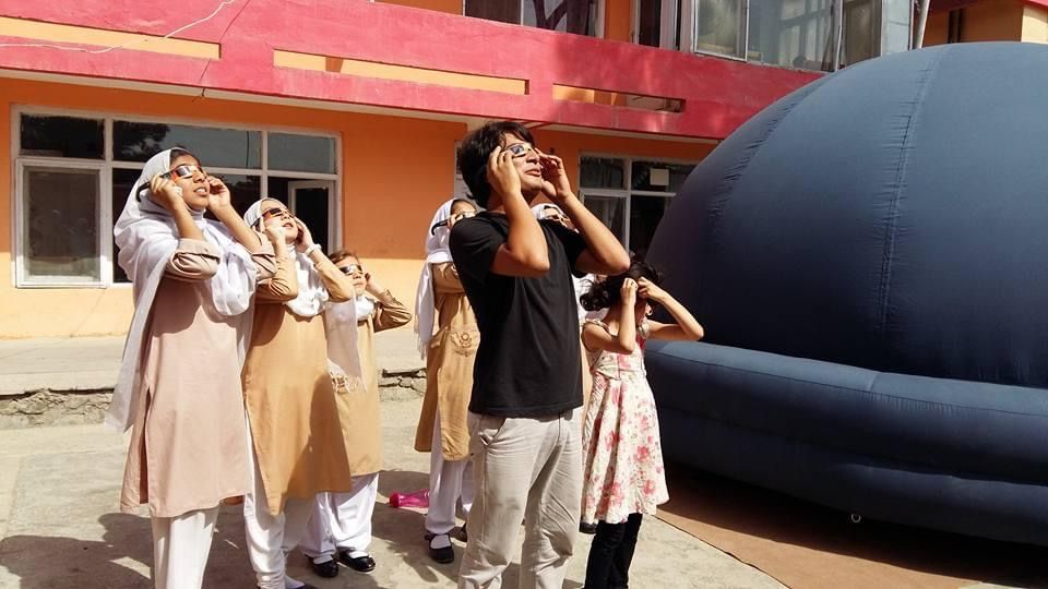 Abraham Amiri and a group of his female students in Afghanistan wearing special glasses look upward