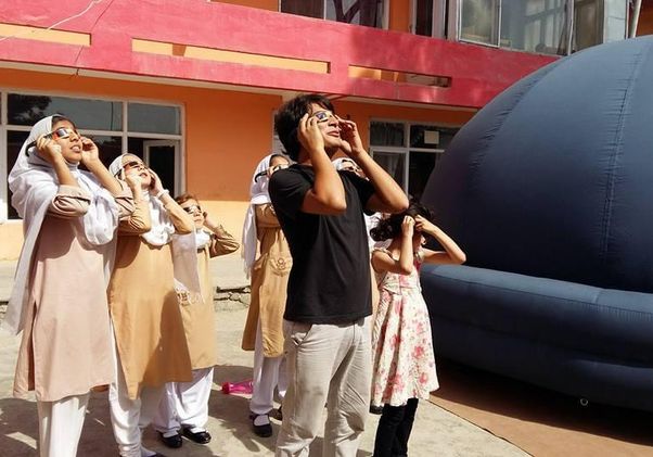 Abraham Amiri and a group of his female students in Afghanistan wearing special glasses look upward