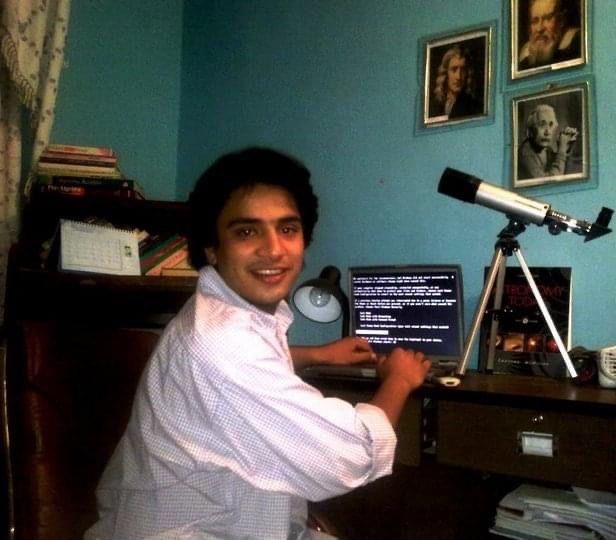 Abraham Amiri sits and a desk with a laptop and small telescope