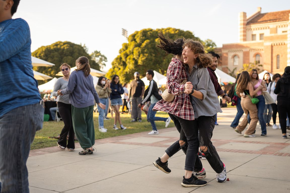 Students laughing and dancing in pairs during the Latinx Welcome event in Wilson Plaza