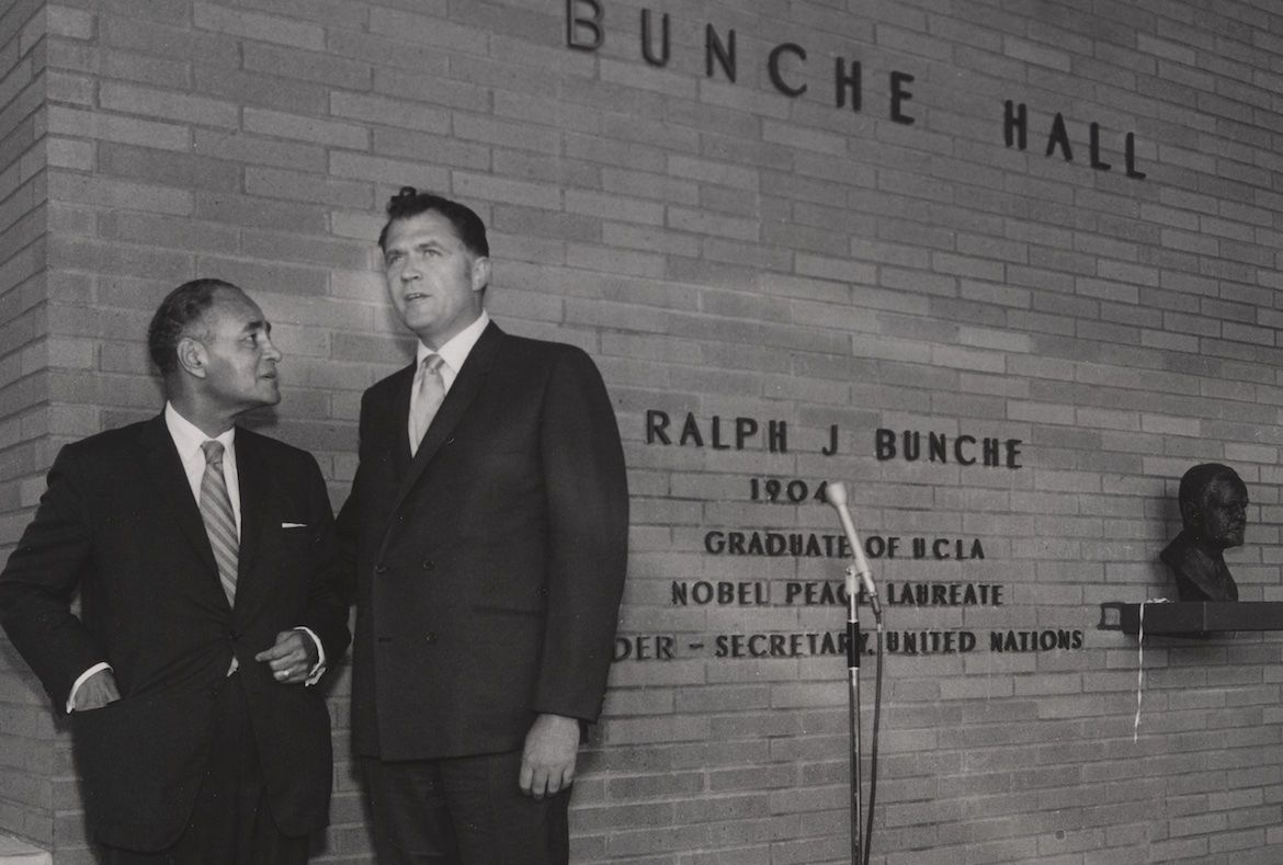Black-and-white photo featuring Charles E. Young and Ralph J. Bunche to the far left, with a wall reading “Bunche Hall” to the right