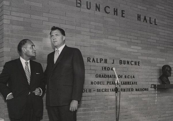 Black-and-white photo featuring Charles E. Young and Ralph J. Bunche to the far left, with a wall reading “Bunche Hall” to the right