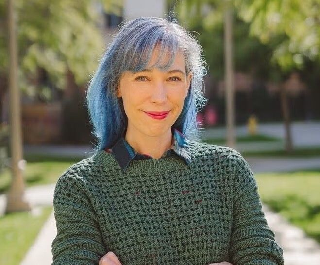 Color head-and-shoulders photo of Michelle Liu Carriger in 2023 standing with arms crossed on a path