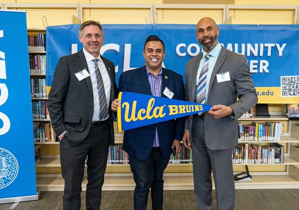 Left to right: Sean Teer, principal of Downtown Magnets High School; California Assemblymember Mark Gonzalez; and UCLA Interim Chancellor Darnell Hunt. Gonzalez and Hunt holds a UCLA penant; all three stand in front of a “UCLA community partner” banner.