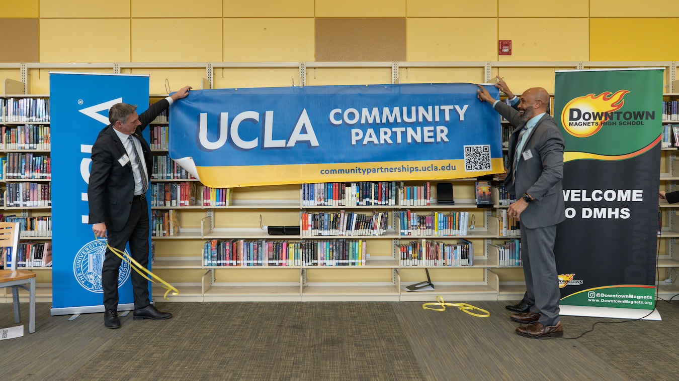 Downtown Magnets principal Sean Teer (left) and Darnell Hunt hang the new UCLA community partnership banner in the school library.