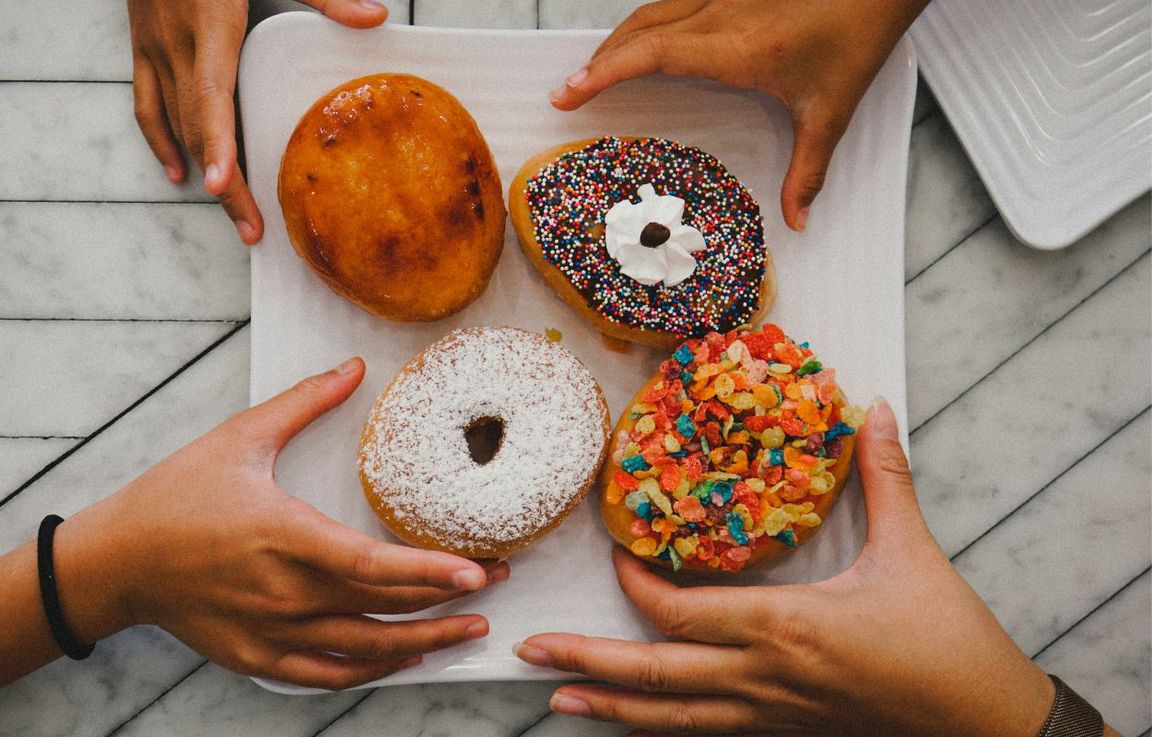 Four hands reaching for designer doughnuts