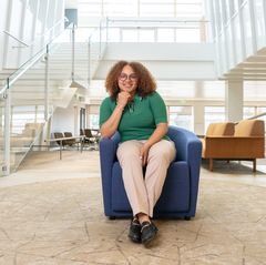 Brija Johnson sits on a blue chair for a portrait in the strategic plan spotlight series
