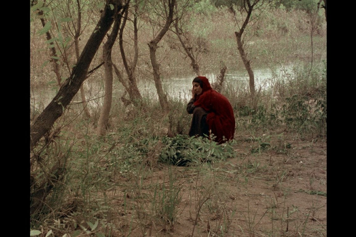 Still image from “The Sealed Soil” (1977) featuring a woman in red clothing sitting on the ground near a river