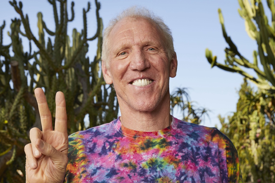 Bill Walton in tie-dye shirt hold in front of cactus holding up peace sign