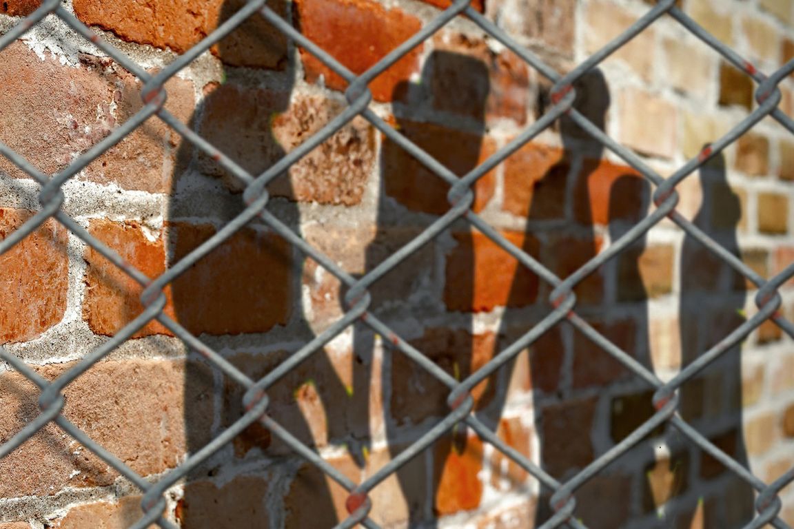 Shadows against brick wall with chain-link fence in foreground