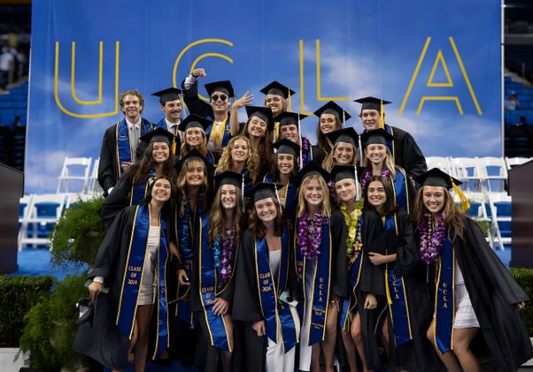About two dozen graduates pose in front of UCLA sign in Pauley Pavilion