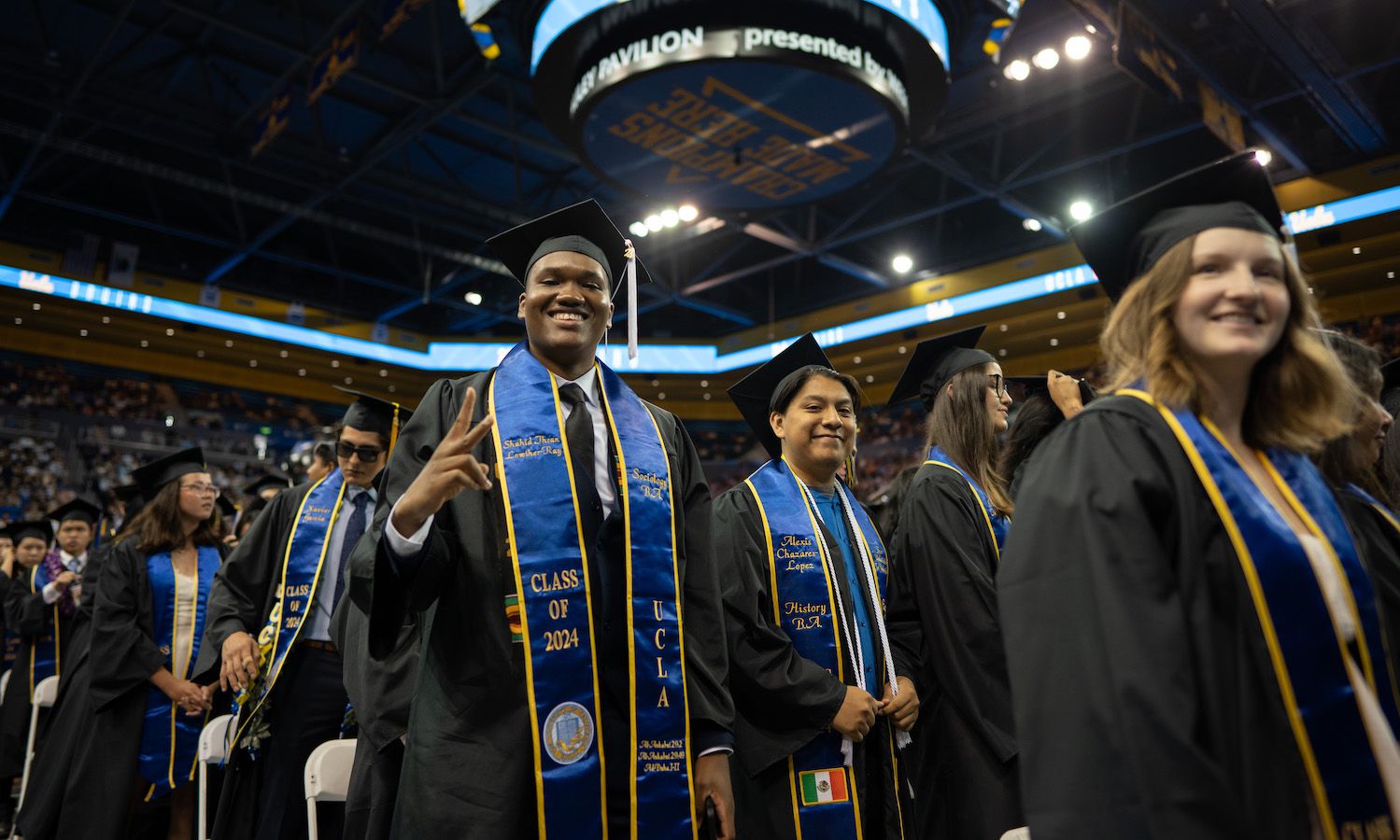 Student throws up peace sign while standing with fellow graduates in Pauley Pavilion