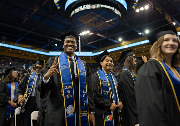 Student throws up peace sign while standing with fellow graduates in Pauley Pavilion