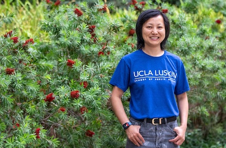 Wide shot of Emily Wang in front of ivy wearing blue UCLA Luskin T-shirt.